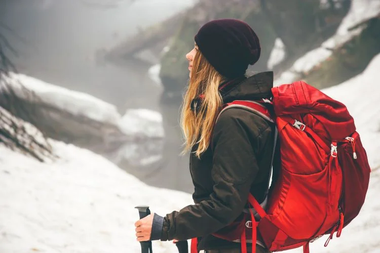 Une femme en montagne avec un sac à dos et des vêtements de montagnes pour l'hiver.