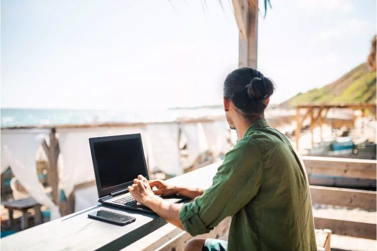 Nomade digital dans un café zen bord de plage travaillant sur son ordinateur portable